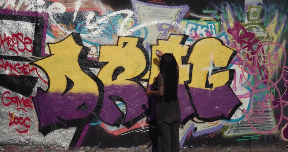 Black man doing graffiti in a wall outdoors during a sunny day