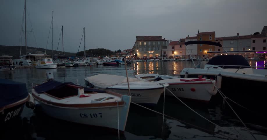Boats bob in the water as people more along the waterfront after dusk