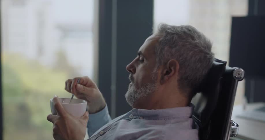 Man leisurely sitting on an office chair at work eating cookies and drinking coffee