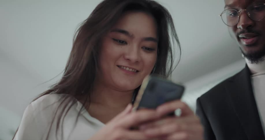 A woman is holding her cell phone and looking at it when a man comes over and speaks to her