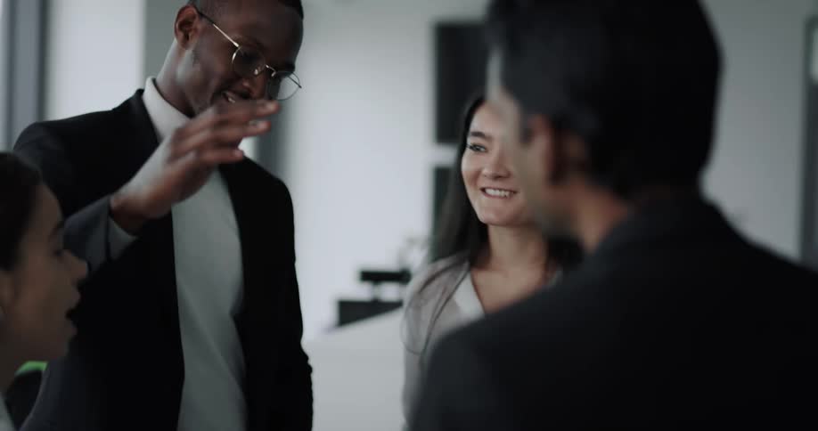 A group of people talk and high five one another while standing together in an office during the day