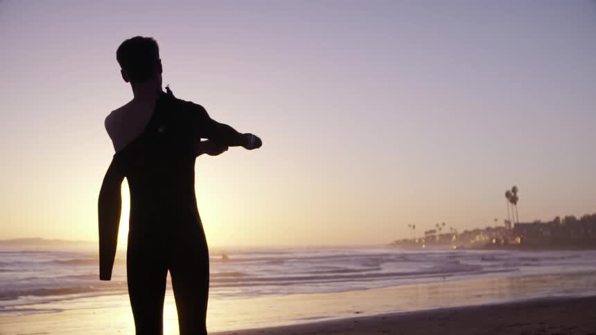A man puts on a wet suit at sunset
