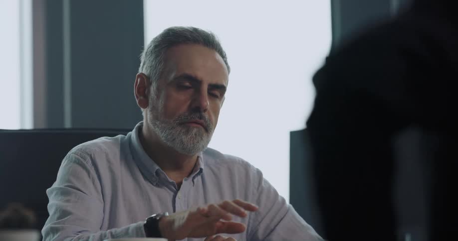 Man listening to business suited man talk encourages the other man to leave and shakes his head before sipping coffee