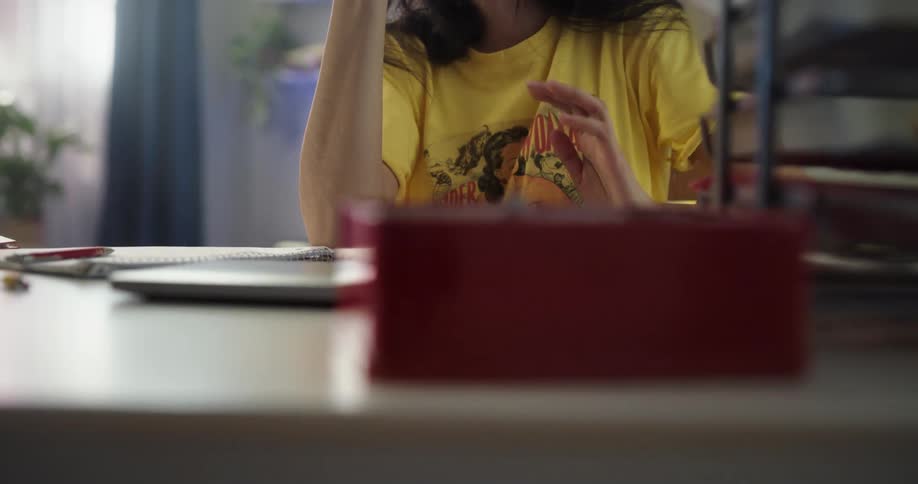 Young asian woman getting up from the couch sitting down at the desk and opening up her laptop lid