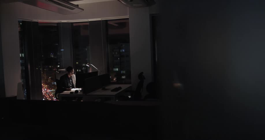 A man in a large office sitting working alone at night