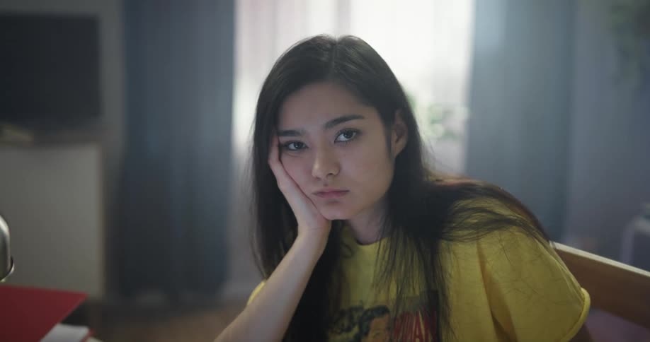 Young woman sitting at a desk in her room looking at the camera
