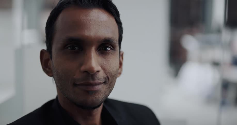 Man with black blazer jacket smiles at camera in the office