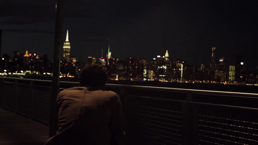 A man looks at the city across the water at night
