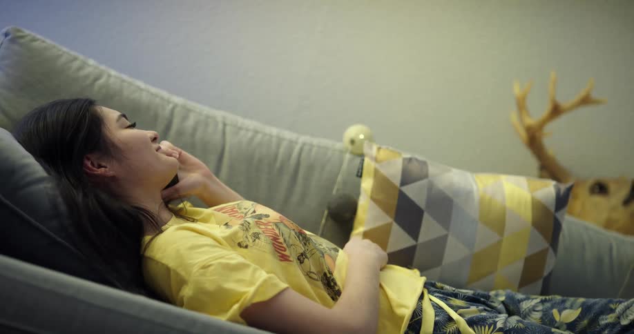 A woman talks on a smartphone while lying on a sofa