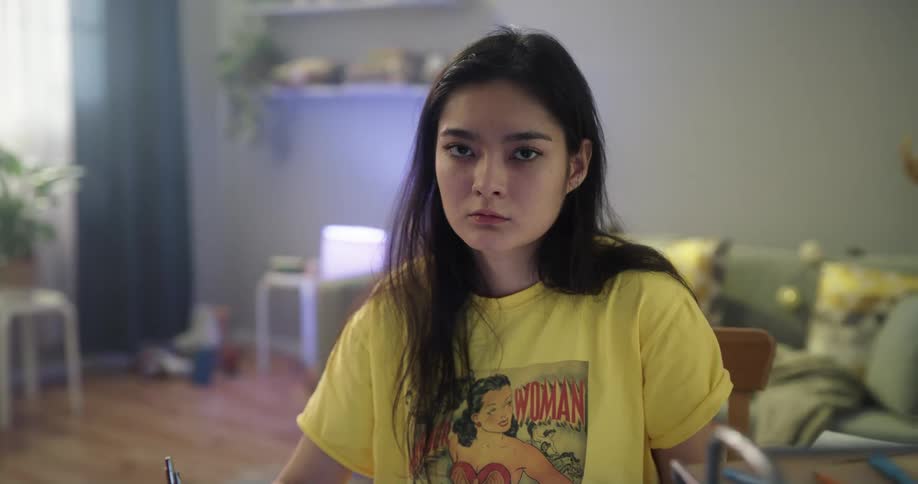 A teenager sits at a desk surrounded by a messy room