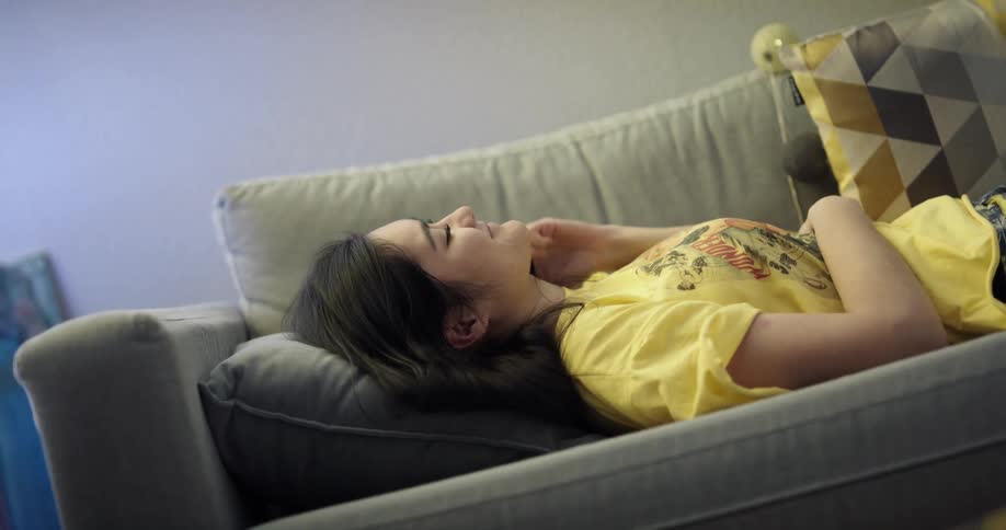 Woman with dark long hair lies on couch and answers call on smartphone in living room at home