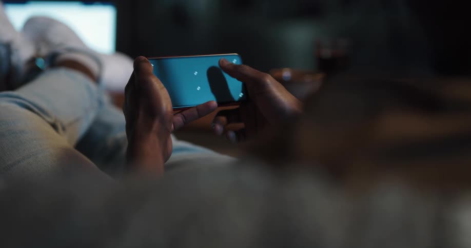 Male relaxing in the dark scrolling social media on his cell phone