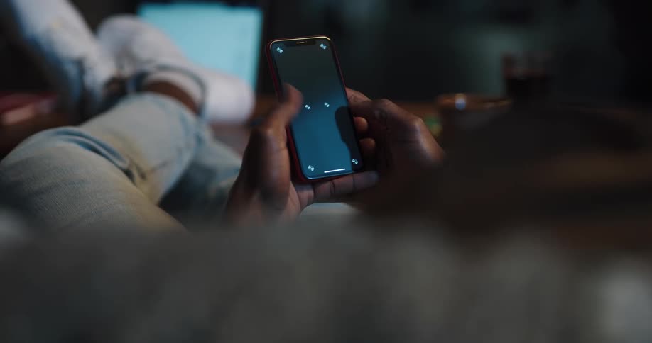 A person reclines on their couch while using their fingers to swipe on the screen of their smart phone