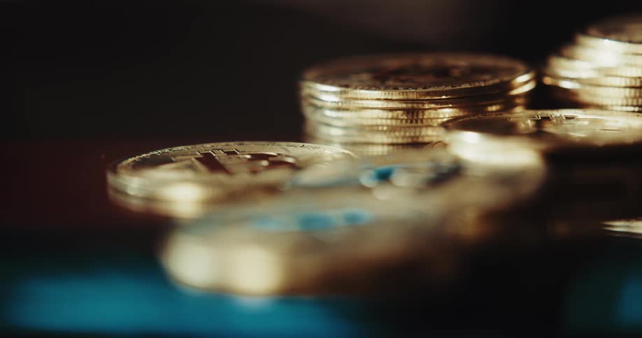 Close up of the shiny engraved surface of golden bitcoin physical coins over a reflecting surface