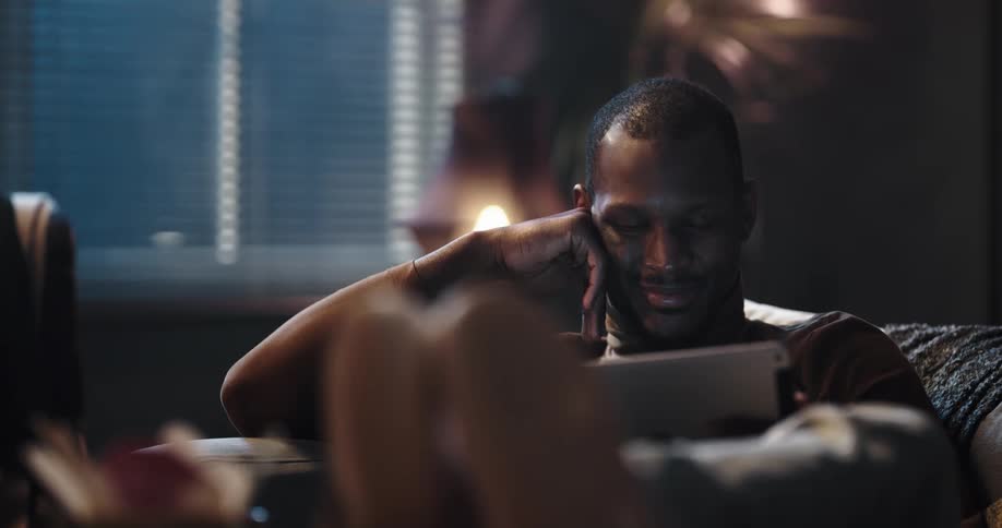 Black man sitting on the couch with his legs up watching something on his ipad