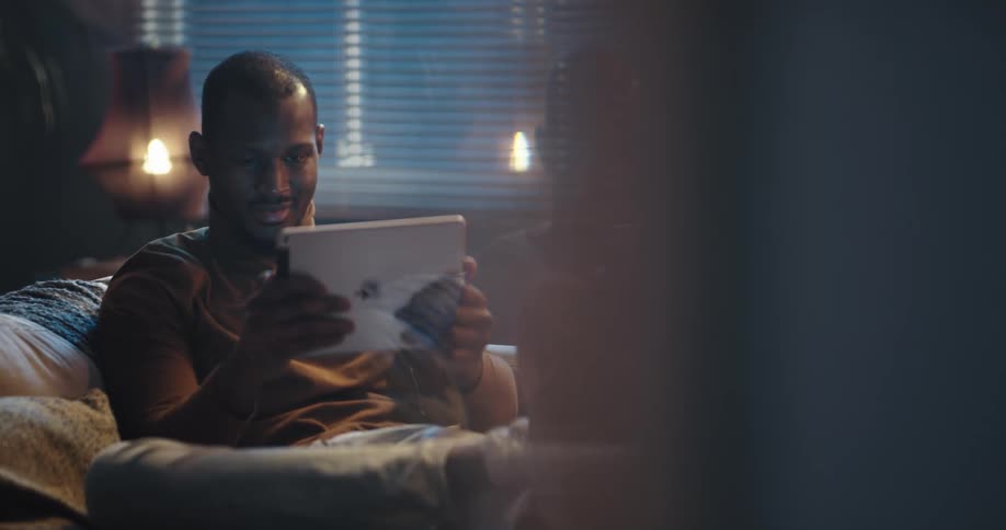 Man sitting on the couch inside his house playing a game on his ipad