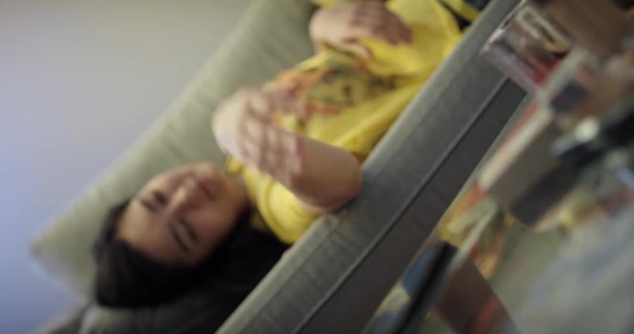 A woman talking on the phone while laying on the sofa sets her phone on the coffee table