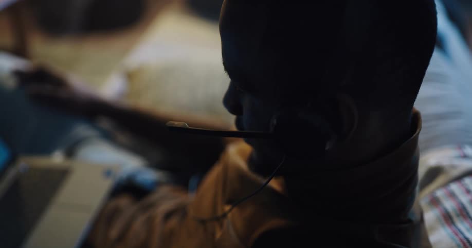 Black man sitting on the couch talking to someone on his headset with his laptop on his lap