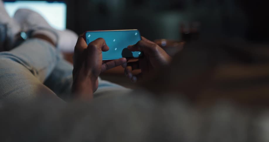 Black man lying down in the couch with his legs up playing a game on his smartphone