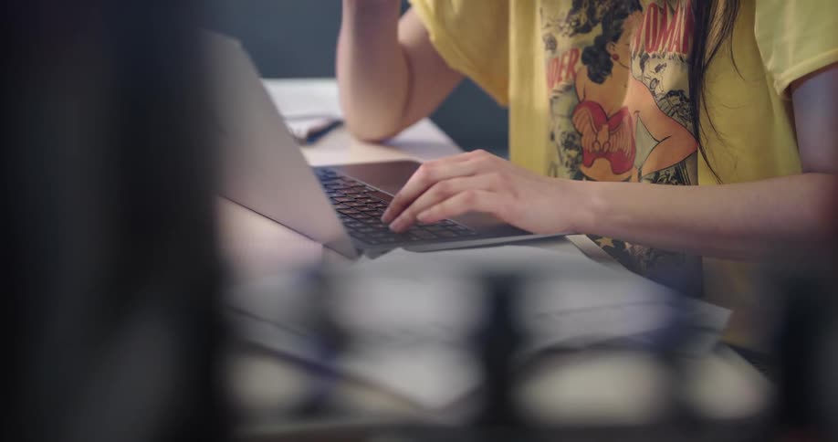 Young asian woman sitting at the desk using her laptop and handling a stack of papers