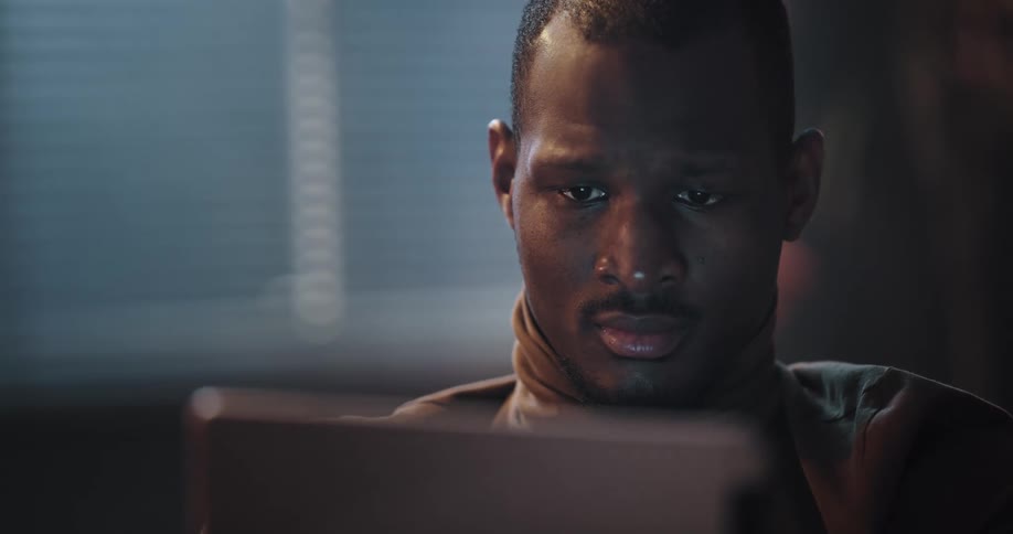 A man playing a game on his computer tablet while sitting indoors lowers the tablet and shakes his head in disappointment