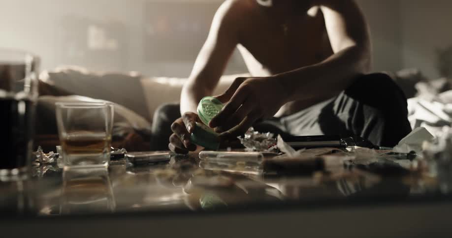 A man grinds marijuana while sitting on the couch