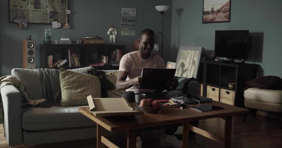 Man sitting on the couch smiles as he opens vinyl record with television and turntable in the background