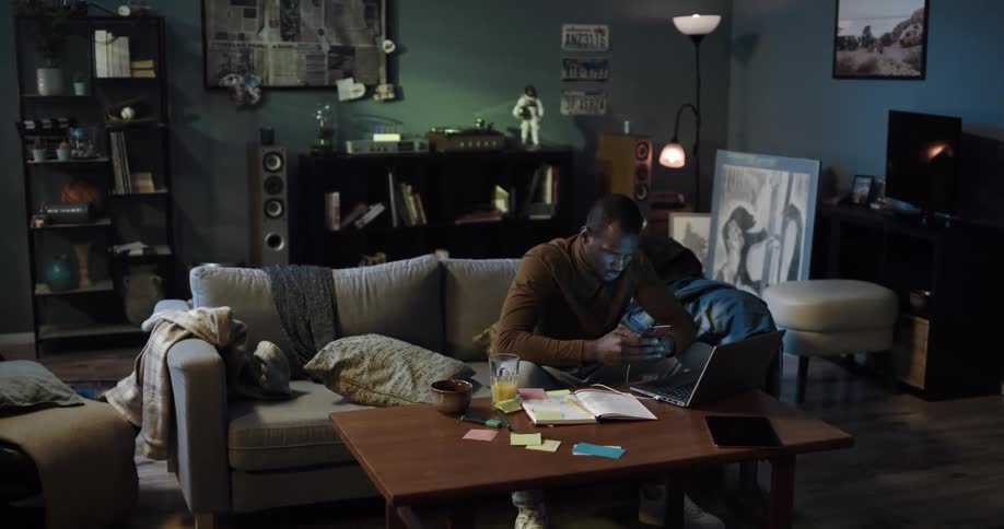 Man sitting on the couch at home takes handwritten notes from the phone into a notepad