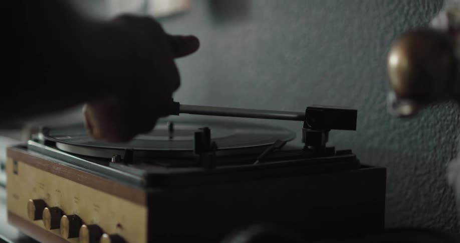 Black man putting a vinyl record in the record player and then grabbing his headphone