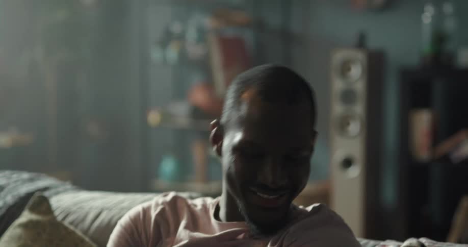 Man smiles and gestures while sitting in living room and listening to music