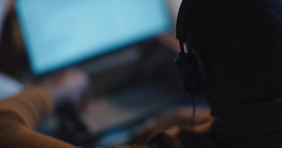 Man wearing headphones and brown turtleneck sweater sits on sofa and uses laptop in living room at home