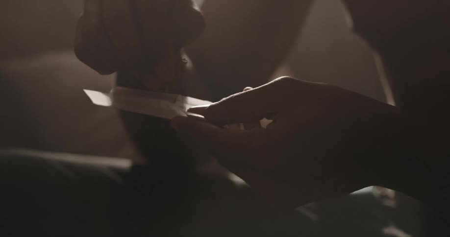 Shirtless black man rolling a marijuana joint