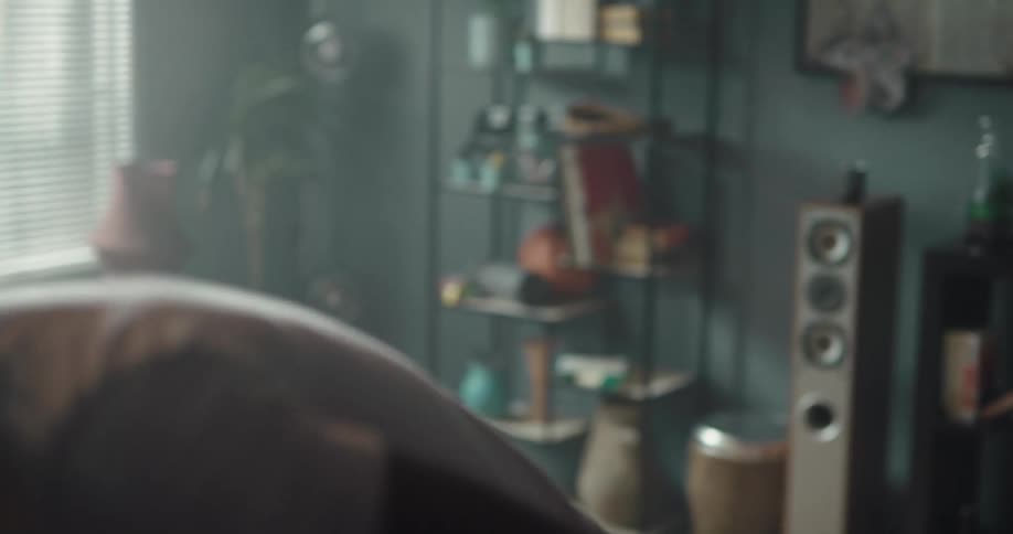 Man putting on his headphone and sitting on the couch in his living room while moving and dancing to the sound of the music