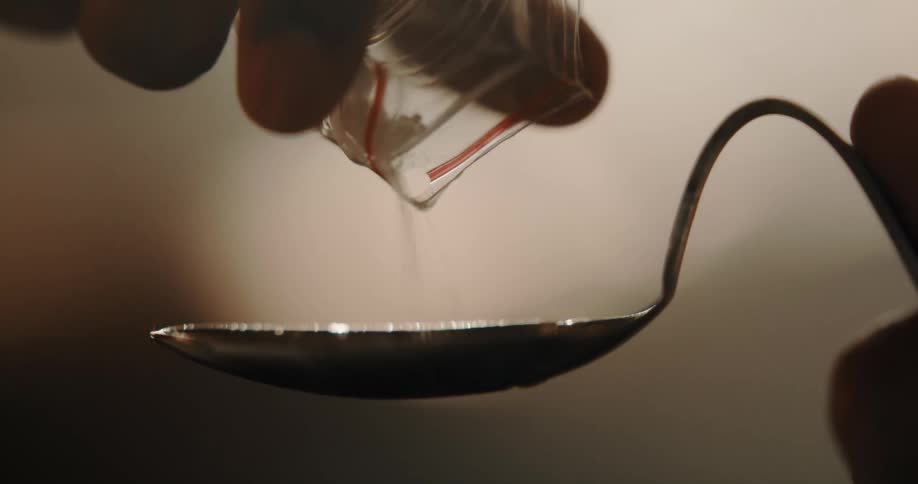 Man filling a bent spoon with drugs inside a dimly lit room