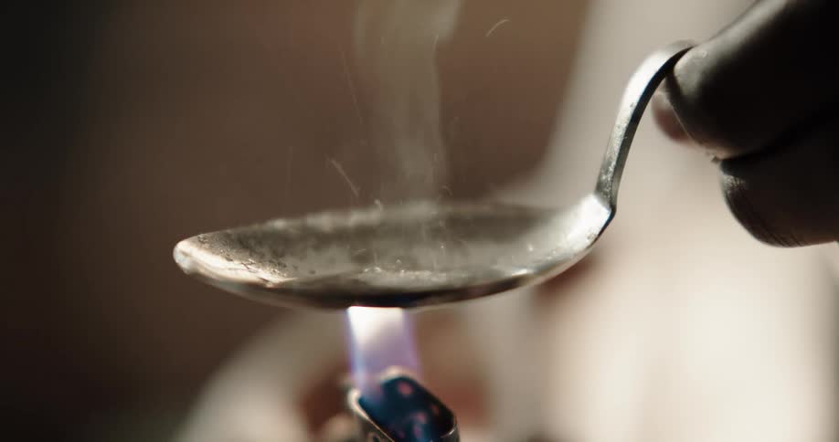 Drug addict heating meth with a lighter under metal spoon