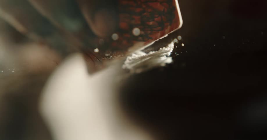 A person pours some cocaine out on a surface and starts chopping it with a card