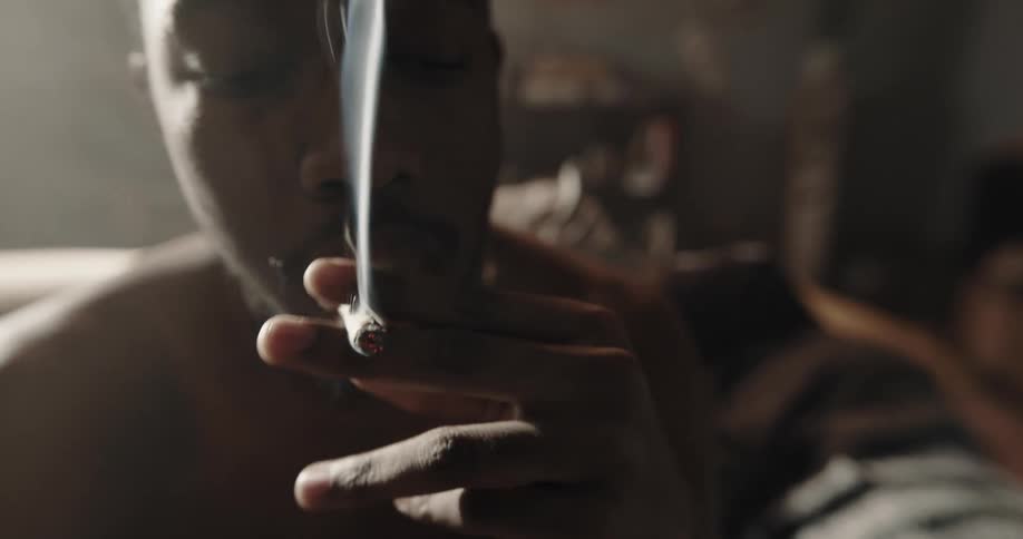 Shirtless man sitting on couch smokes cigarette and holds lighter