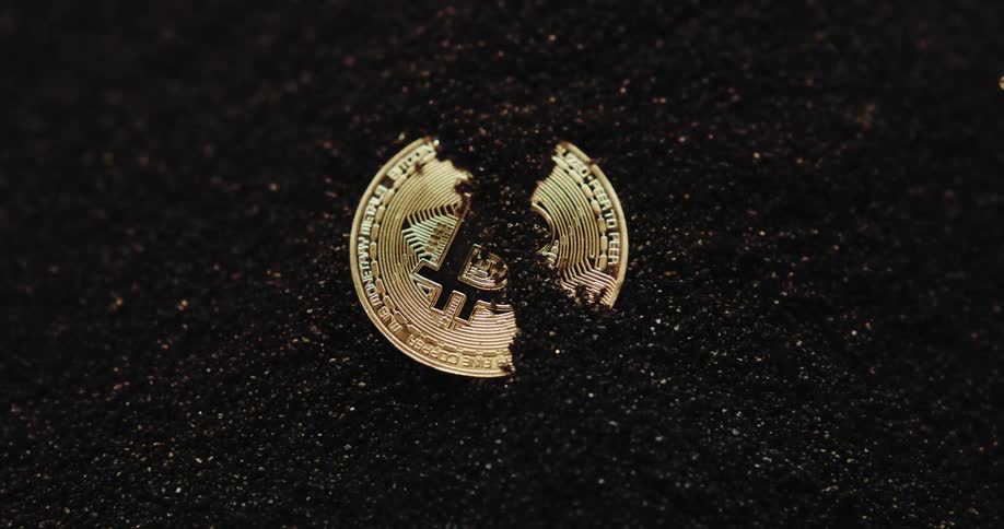 Close up of the shiny engraved surface of golden bitcoin physical coins over dark sand blowing in the wind