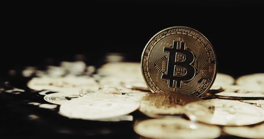 One bitcoin stands on edge as other gold bitcoins are lying in moving water