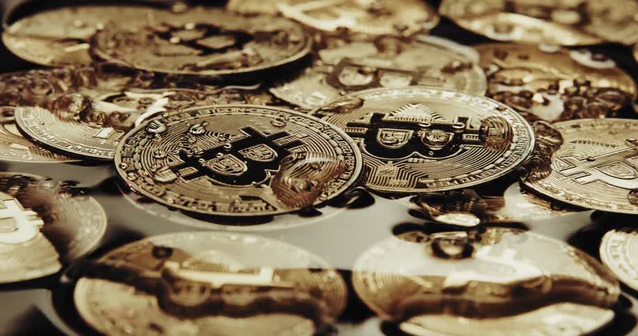 Close up of water running over the shiny engraved surface of golden bitcoin physical coins