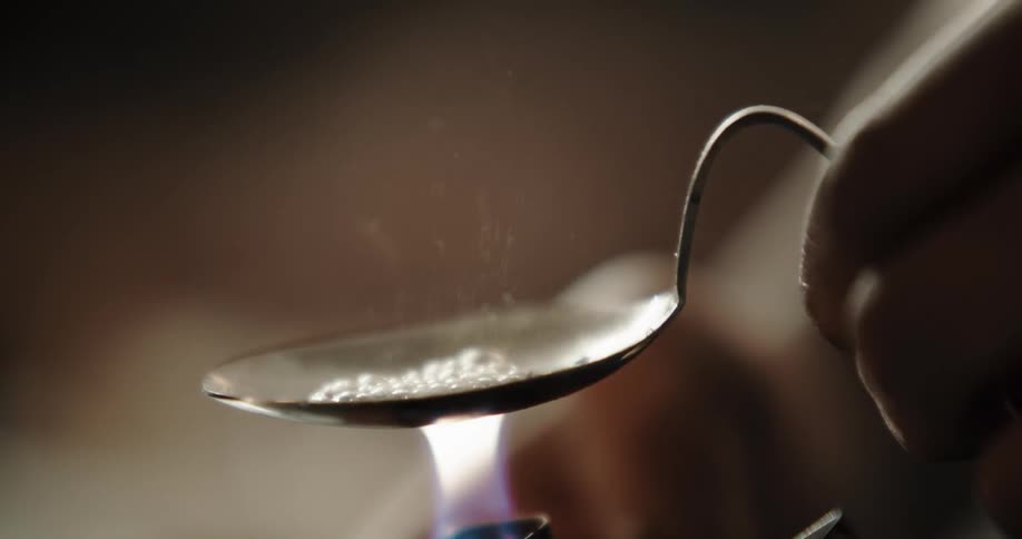 A person holds a bent spoon over a flame from a lighter to heat some illicit drugs