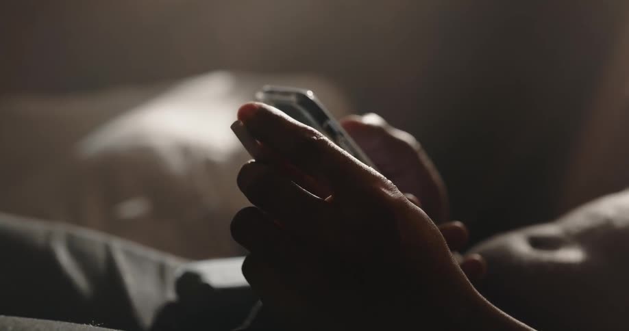Man resting on a couch in the living room at home reading on his phone while spinning drugs on his hand