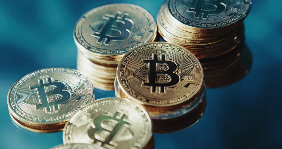 Multiple stacks of coins with the bitcoin logo on them are atop a reflective surface
