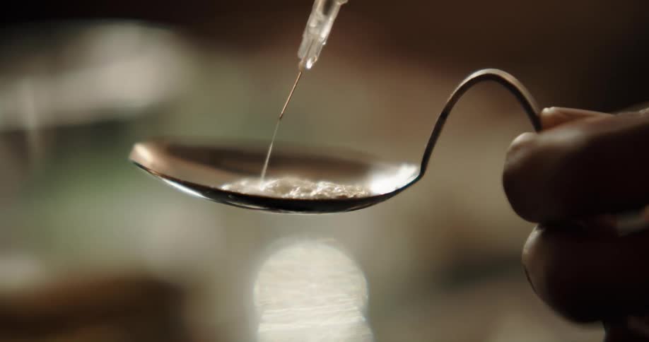 Person adds liquid from hypodermic to illegal substance in crack spoon