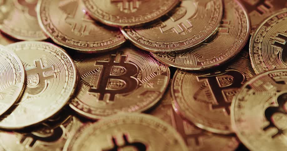 A number of shiny coins with the bitcoin logo on them are piled atop each other