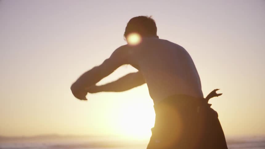 A surfer stretching before pulling his wetsuit up his torso