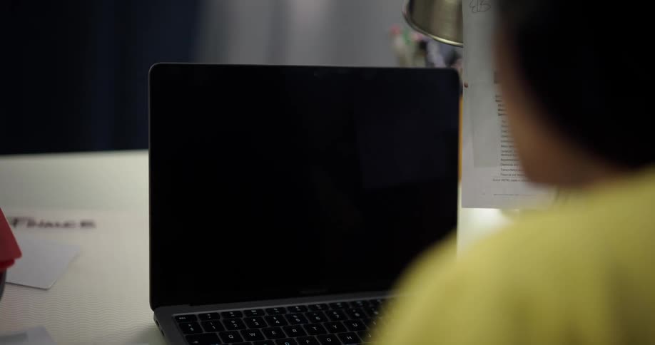 Woman holds a pen in her hand as she looks at text on a paper then she begins to type on a laptop