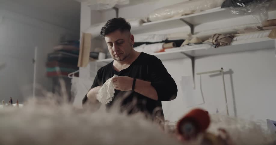 Fashion designer uses a small scissor to cut a piece of cloth in a workshop