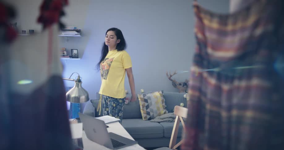 Bored and tired woman with yellow and blue pajamas stretches and goes on to work on laptop