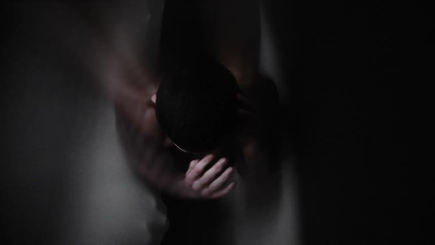 Warped footage of a shirtless scared man inside a dimly lit room